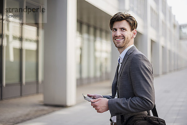 Smiling businessman in the city with bag and tablet