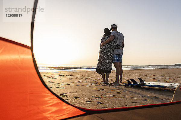 Romantic couple camping on the beach  embracing at sunset