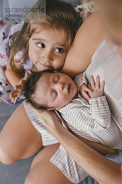 Mother holding her baby close with sister feeling his hair