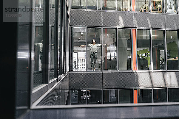 Woman standing at office window  with arms outstretched