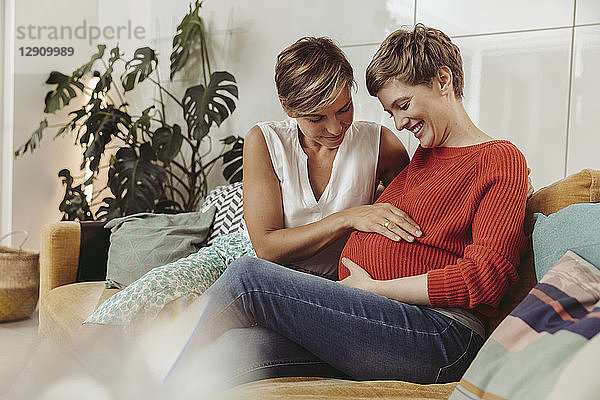 Happy lesbian couple touching belly of the expectant mother