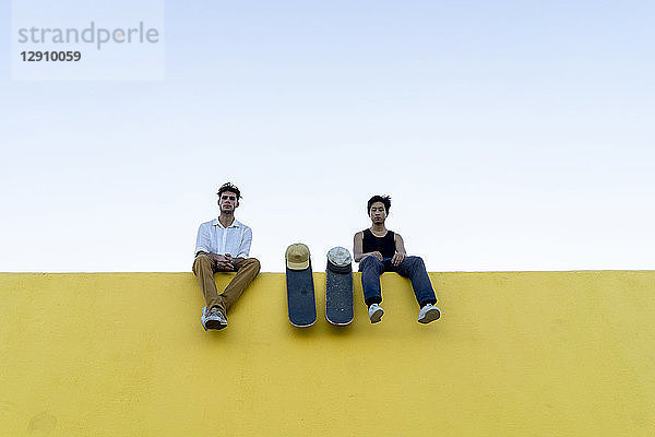 Two young men with skateboards sitting on a high yellow wall