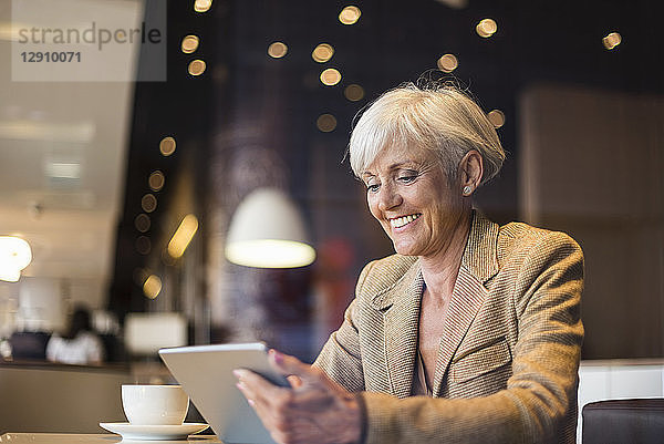 Smiling senior businesswoman using tablet in a cafe