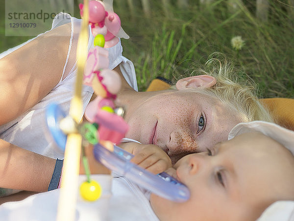 Freckled girl lying with baby girl on blanket on a meadow