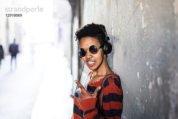 Portrait of young woman listening music with headphones showing Rock And Roll Sign
