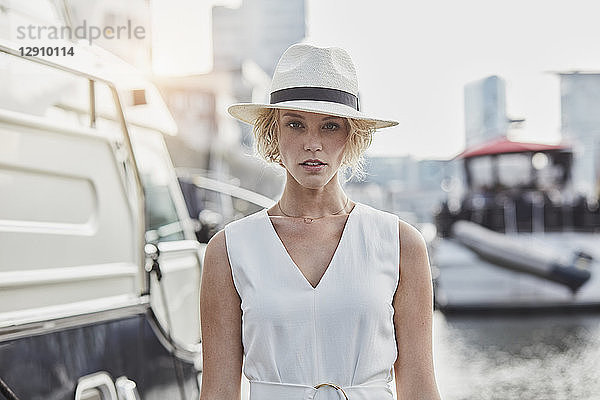 Portrait of serious young woman wearing a hat at a marina next to a yacht