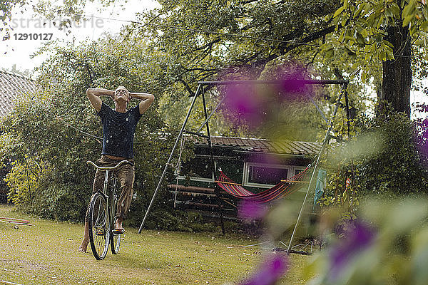 Mature man with bicycle enjoying summer rain in garden