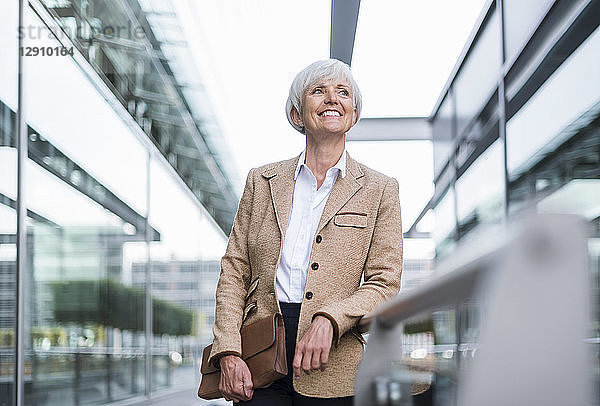 Smiling senior businesswoman leaning on railing in the city looking up