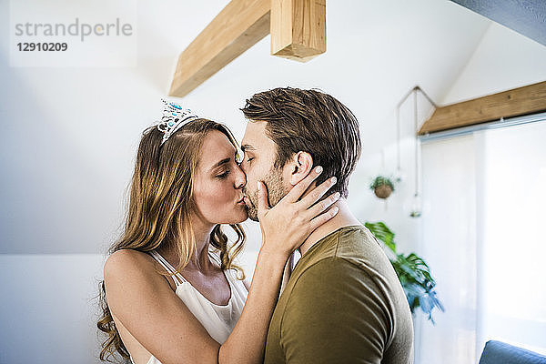 Affectionate couple kissing at home with woman wearing tiara