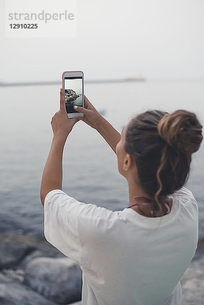 Teenage girl taking pictures of the sea with her smartphone