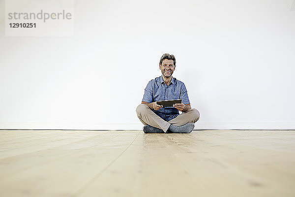 Mature man sitting on ground in empty room  using digital tablet
