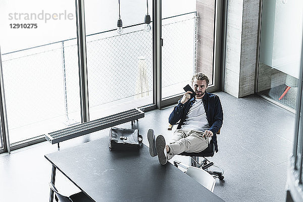 Casual businessman sitting in office with feet up using cell phone