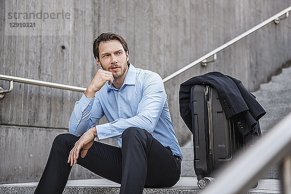 Businessman with rolling suitcase sitting on stairs