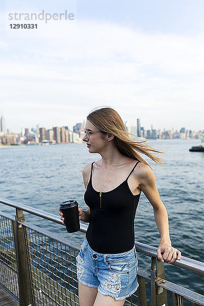 Young woman looking over East River  holding cup of coffee
