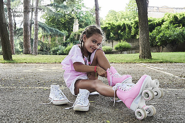 Little girl smiling at camera while putting roller skates on in the park