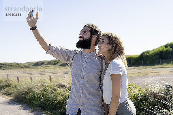 Young couple taking smartphone selfies on the beach