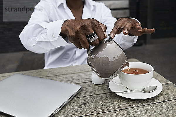 Hands of businesswoman sitting on terrace of a coffee shop pouring tea into a cup