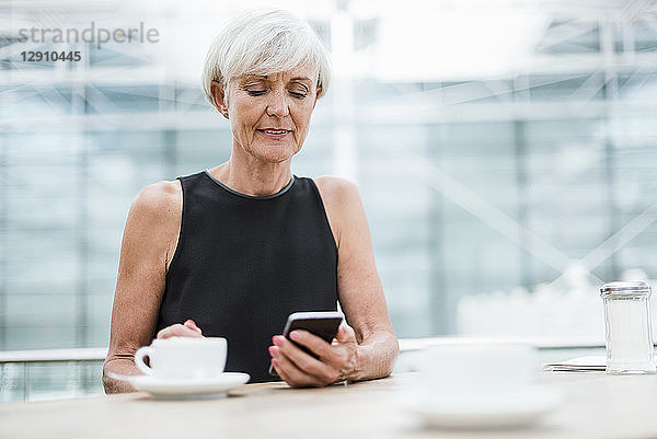 Senior woman using cell phone in a cafe