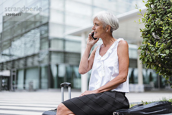 Smiling senior woman with baggage on cell phone in the city