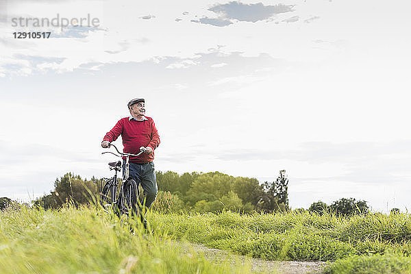 Senior man pushing bicycle in rural landscape