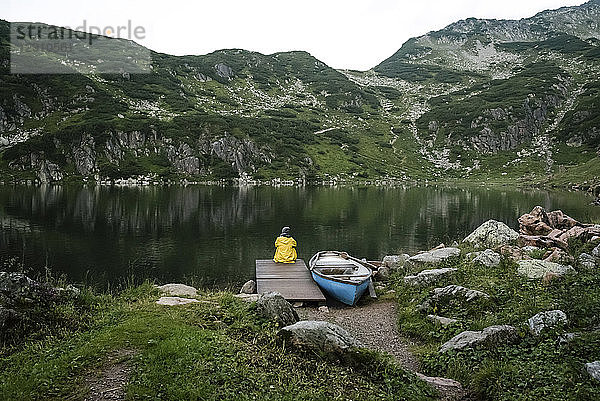 Austria  Tyrol  Fieberbrunn  Wildseeloder  woman sitting at the shore of lake Wildsee next to a boat