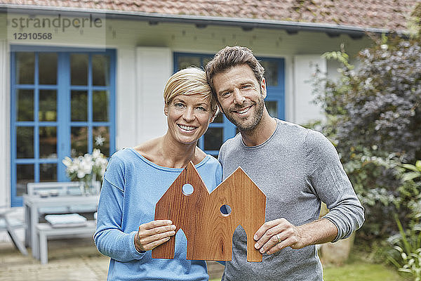 Portrait of smiling couple standing in front of their home holding house model