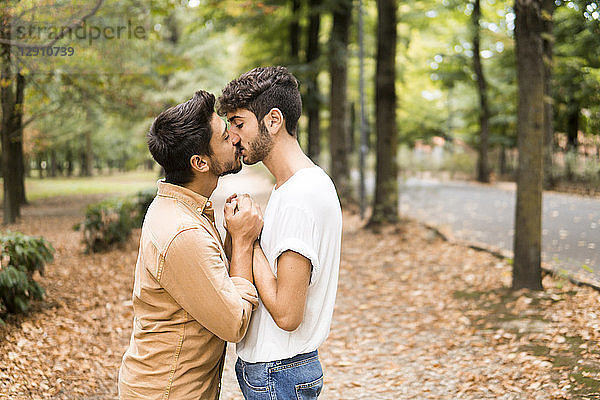 Young gay couple holding hands and kissing in autumnal park