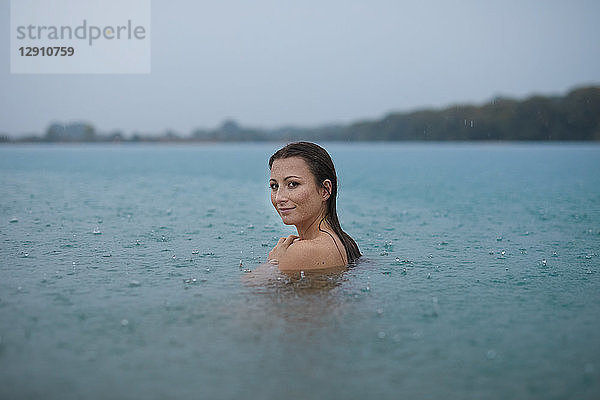 Portrait of smiling young woman bathing in lake on rainy day