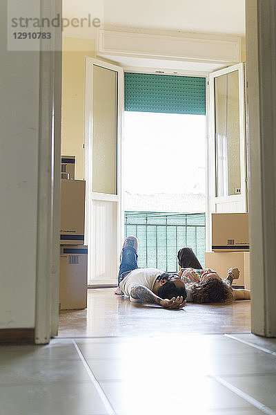 Couple lying side by side on the floor of new home in front of open balcony door