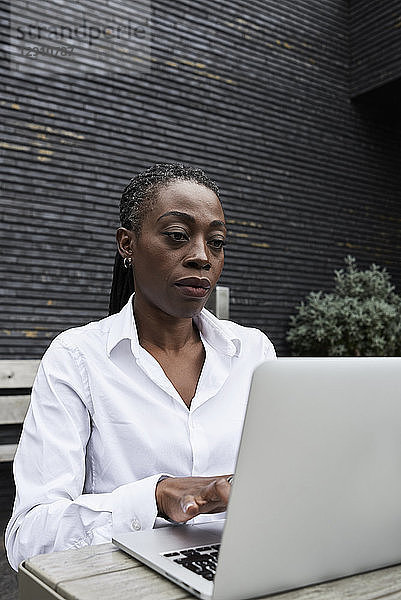 Portrait of businesswoman sitting on terrace of a coffee shop working on laptop