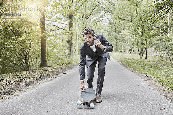 Businessman walking with skateboard and smartphone on rural road