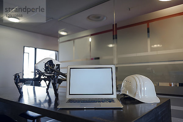 Laptop between hard hat and drone on desk in engineer's office