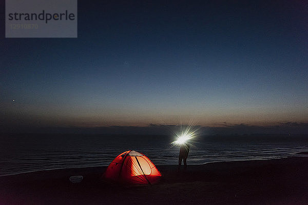 Young man camping on the beach  using flashlight