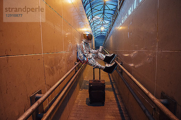 Spaceman in the city at night with rolling suitcase in narrow passageway