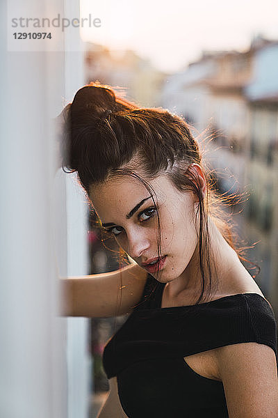Portrait of beautiful young woman on balcony above the city at sunset