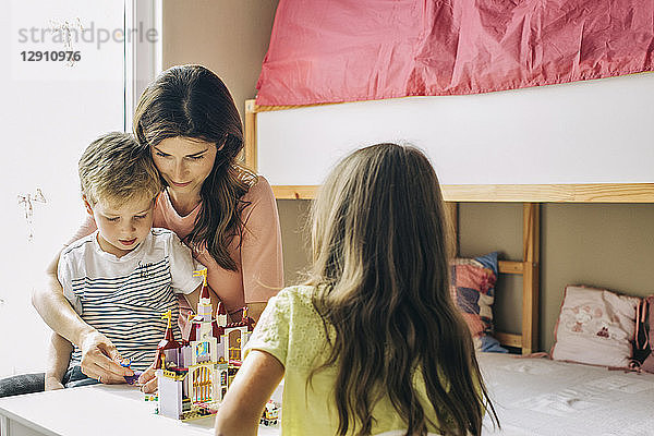 Mother with two children building up toy castle at home