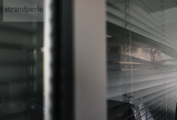 Woman standing by window  spying through blinds