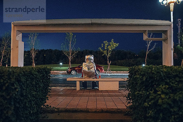 Spaceman sitting on bench at a bus stop at night