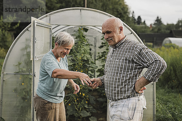 Smiling senior couple in front of green house