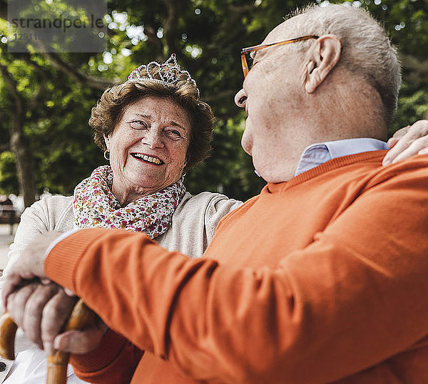 Happy senior couple sitting in park  woman wearing crown