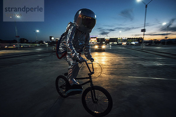 Spaceman in the city at night on parking lot riding bmx bike