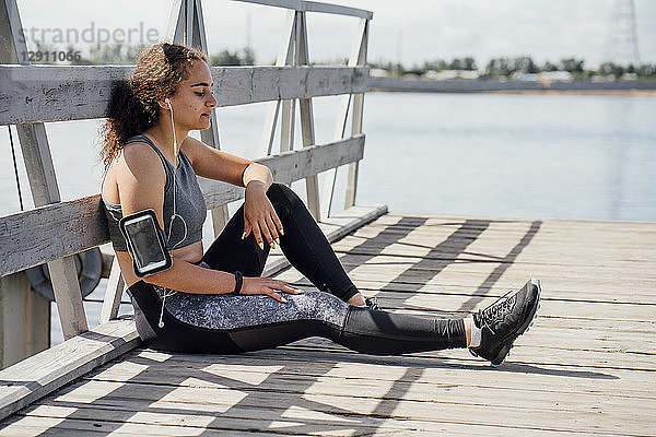 Young athletic woman wearing earbuds resting at the riverside