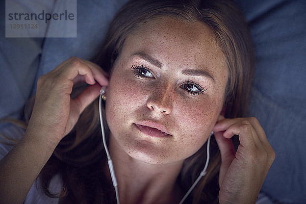 Young woman lying on cushion  listening music with earphones