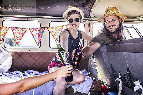 Happy friends inside van clinking bottles