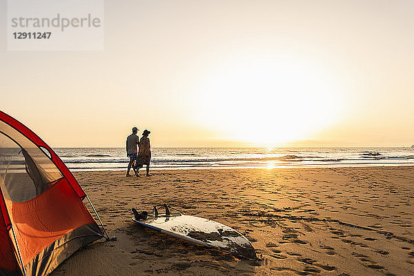 Romantic couple camping on the beach  doing a beach stroll at sunset