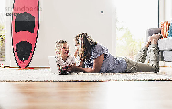 Mother and daughter using laptop  lying on carpet