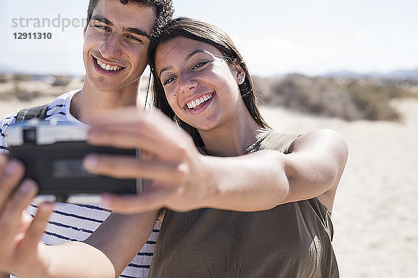 Young couple having fun on the beach  taking smartphone selfies