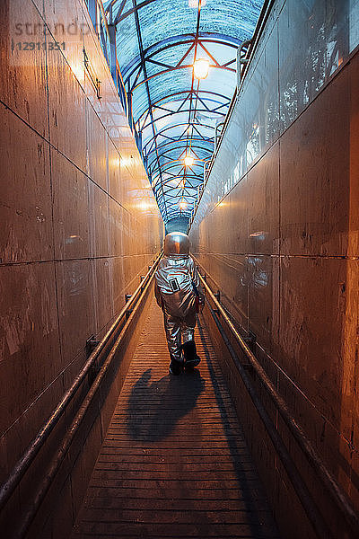 Rear view of spaceman in the city at night walking in narrow passageway