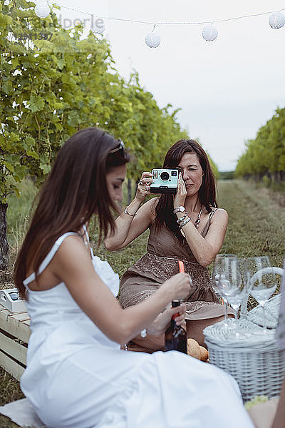 Friends having picnic in a vineyard  one woman taking pictures with instant camera