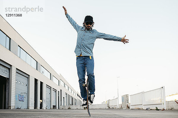 Trendy man in denim and cap skateboarding  standing on skateboard